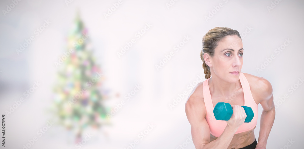 强壮的女人用蓝色哑铃在房间里模糊的圣诞树上做二头肌卷曲