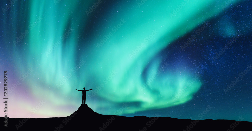 挪威的极光和举起双臂站在石头上的人的侧影。北极光