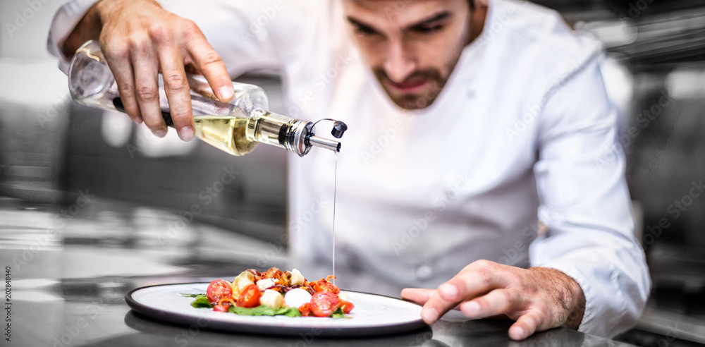 英俊的厨师在商业厨房里为饭菜倒橄榄油