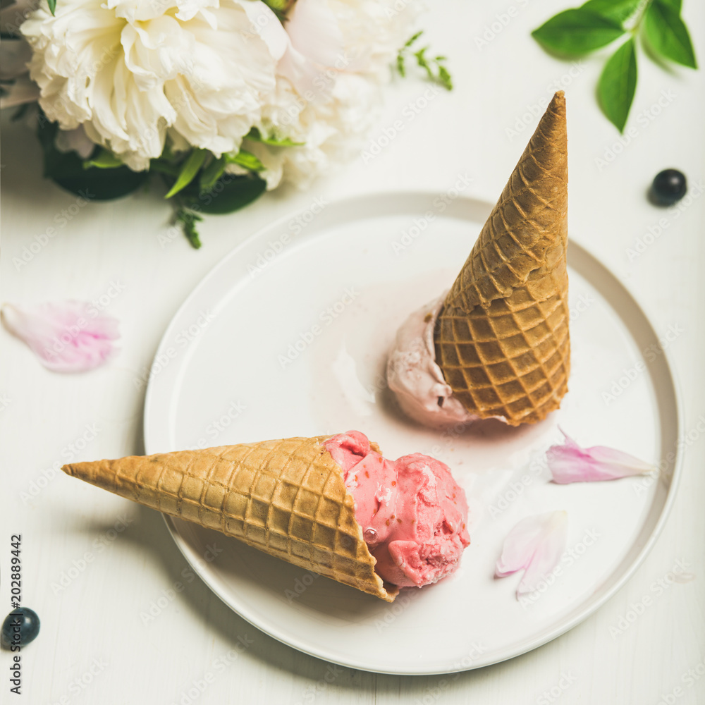 粉色草莓和椰子冰淇淋勺、甜甜筒和牡丹花花束放在盘子里。