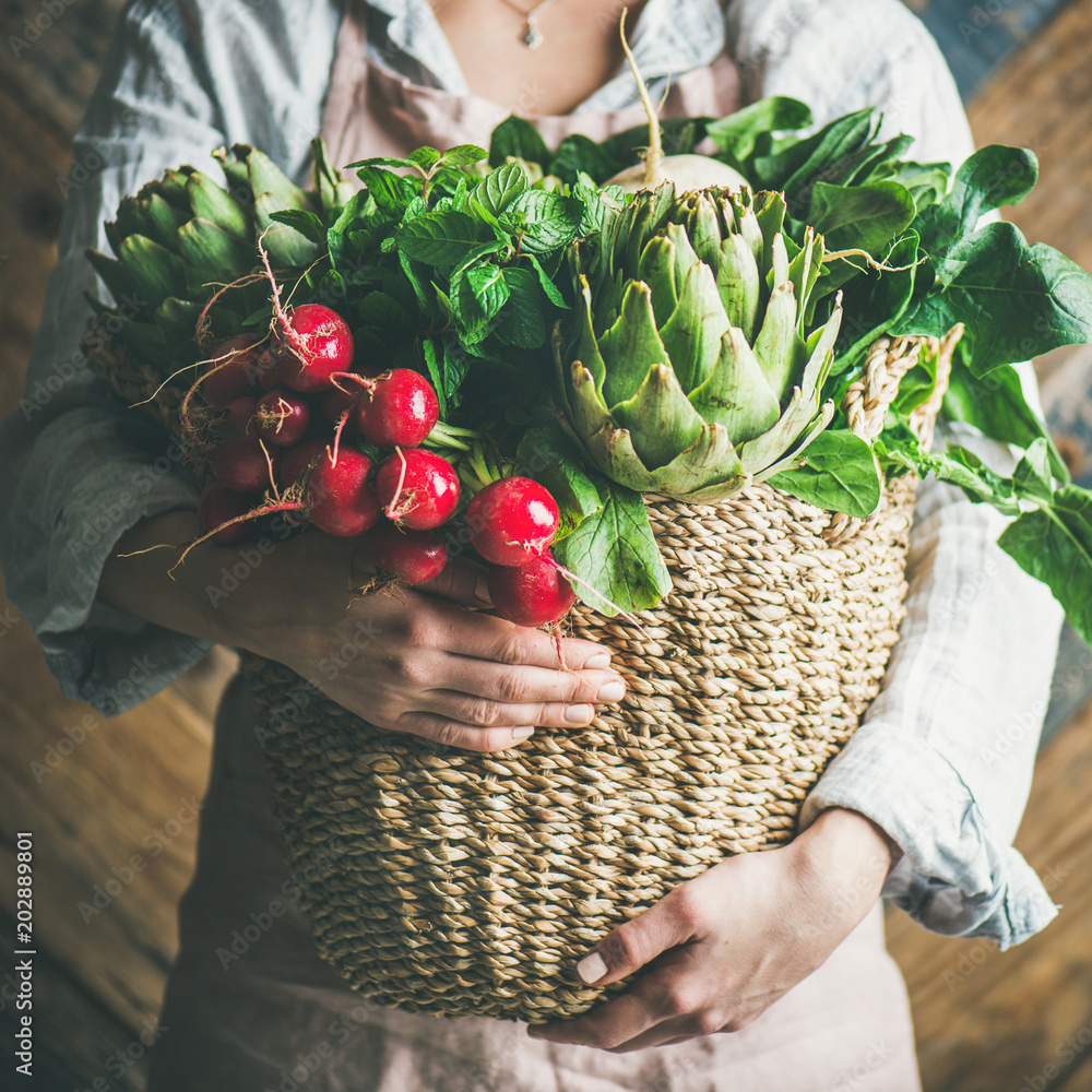 女农民穿着浅色亚麻围裙和衬衫，手里拿着篮子，篮子里装着新鲜的时令蔬菜
