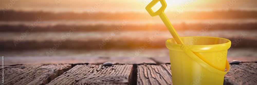 黄色的水桶和铲子与海浪上日落的图像形成对比