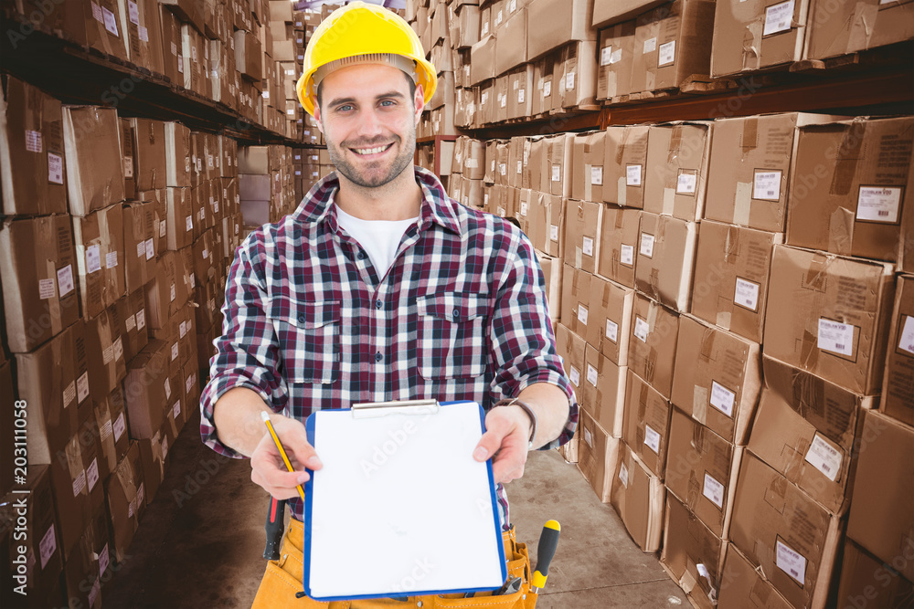 Happy male repairman showing clipboard against boxes in warehouse 