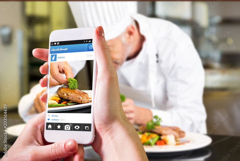 手持智能手机对抗厨房里专心装饰食物的男厨师