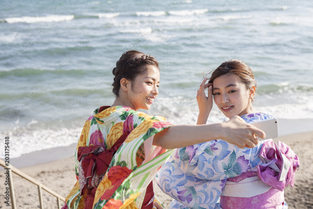 和服女性たちは海辺で写真を撮っている