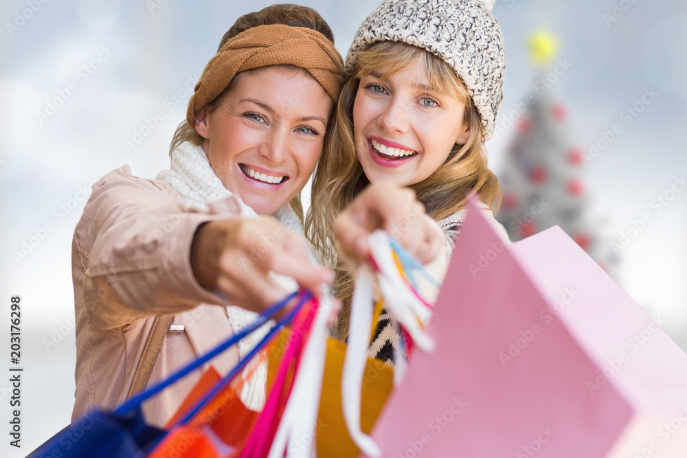 Smiling women looking at camera with shopping bags  against blurry christmas tree in room
