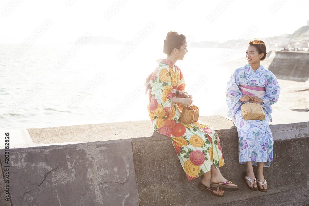 浴衣を着た女性たちは堤防に座っておしゃべりしている
