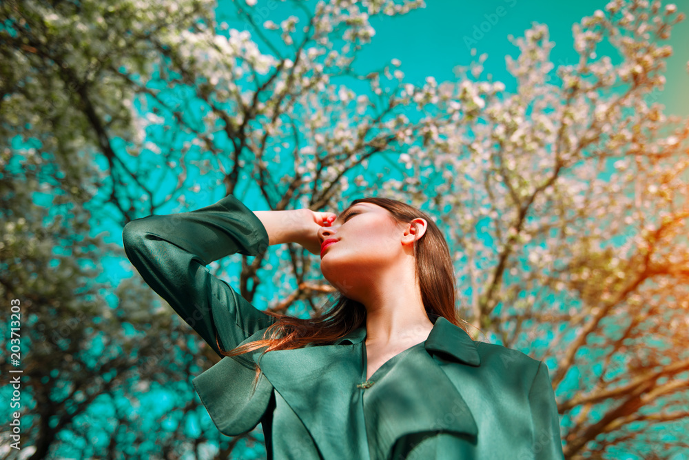 美丽时尚模特女孩在盛开的树上摆姿势，在春天的苹果园里享受大自然。美丽