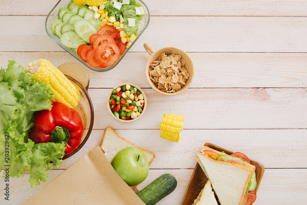 健康的午餐盒，白木背景上有三明治、新鲜蔬菜、水果和坚果。Fro
