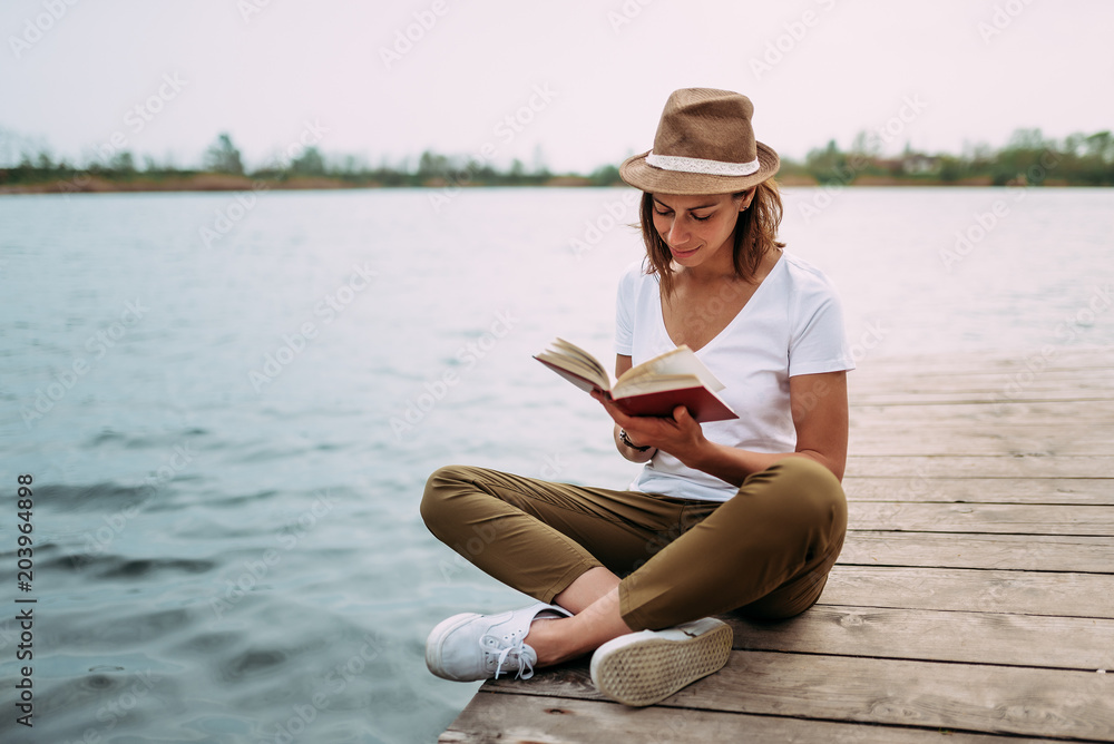 一个女孩坐在一个小木码头上看书的肖像。