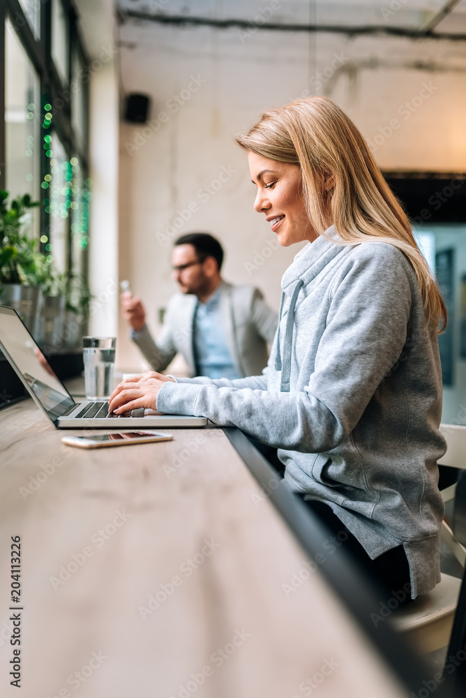 咖啡馆里穿着休闲服的金发美女用笔记本电脑的侧视图。