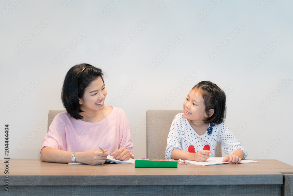 快乐的亚洲家庭。亚洲母亲和女儿一起在书中画画。成年女性帮助