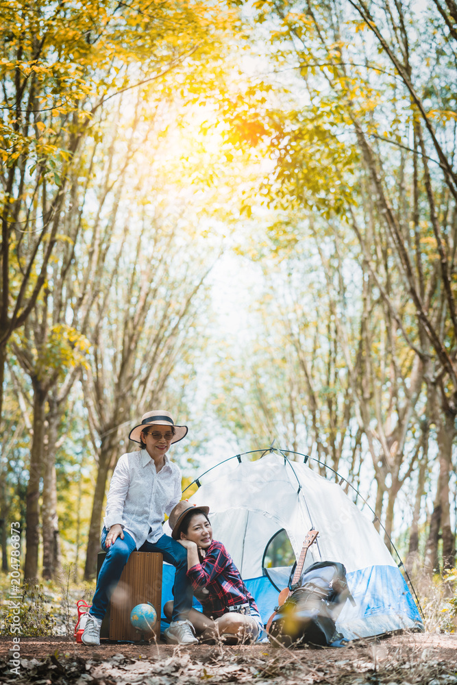 露营概念妈妈和女儿与ukelele一起快乐旅行，并在森林秋季景观中唱歌
