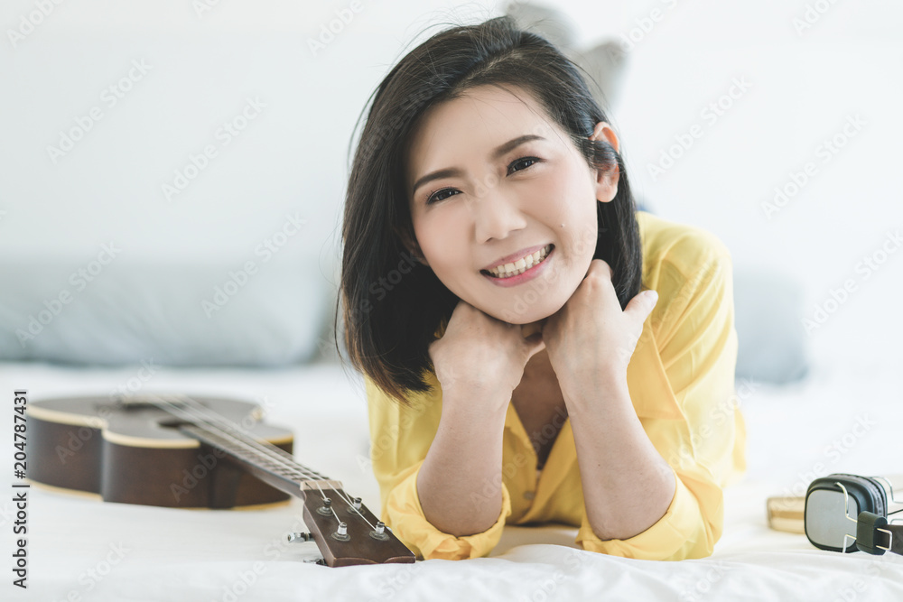 hobby music ukulele with beautiful asian woman in yellow shirt with happiness moment  on bed white r