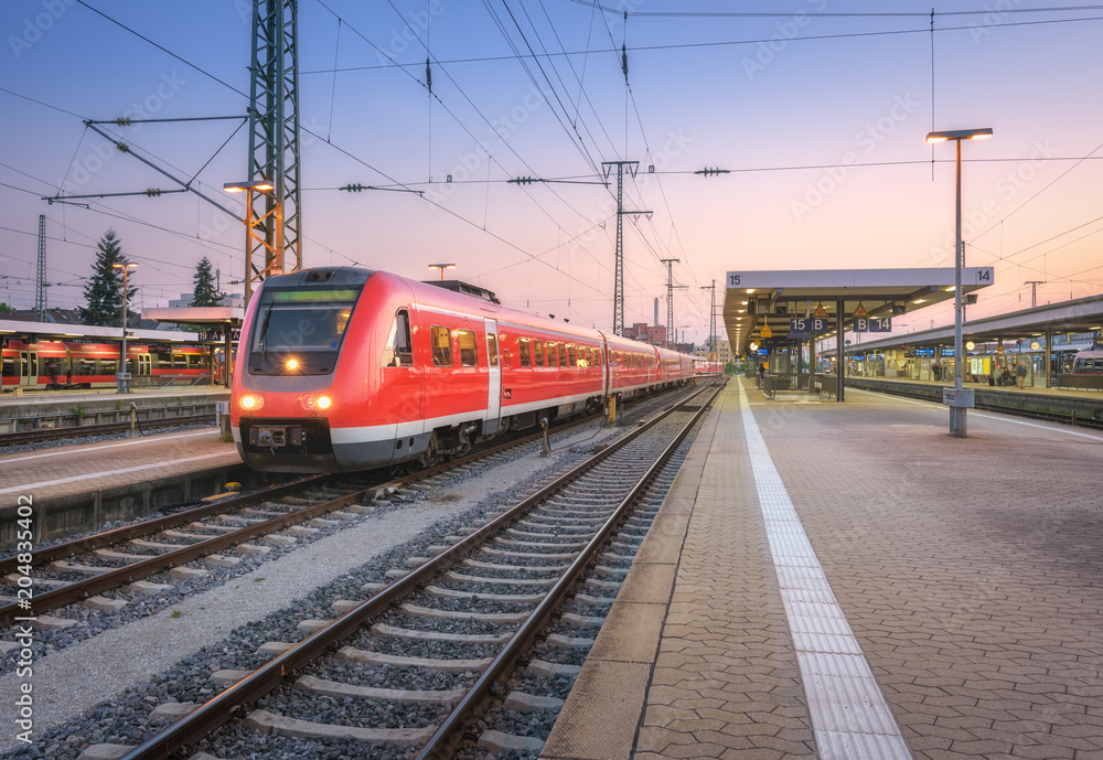 High speed red train on the railway station at sunset. Nuremberg, Germany. Colorful urban landscape.