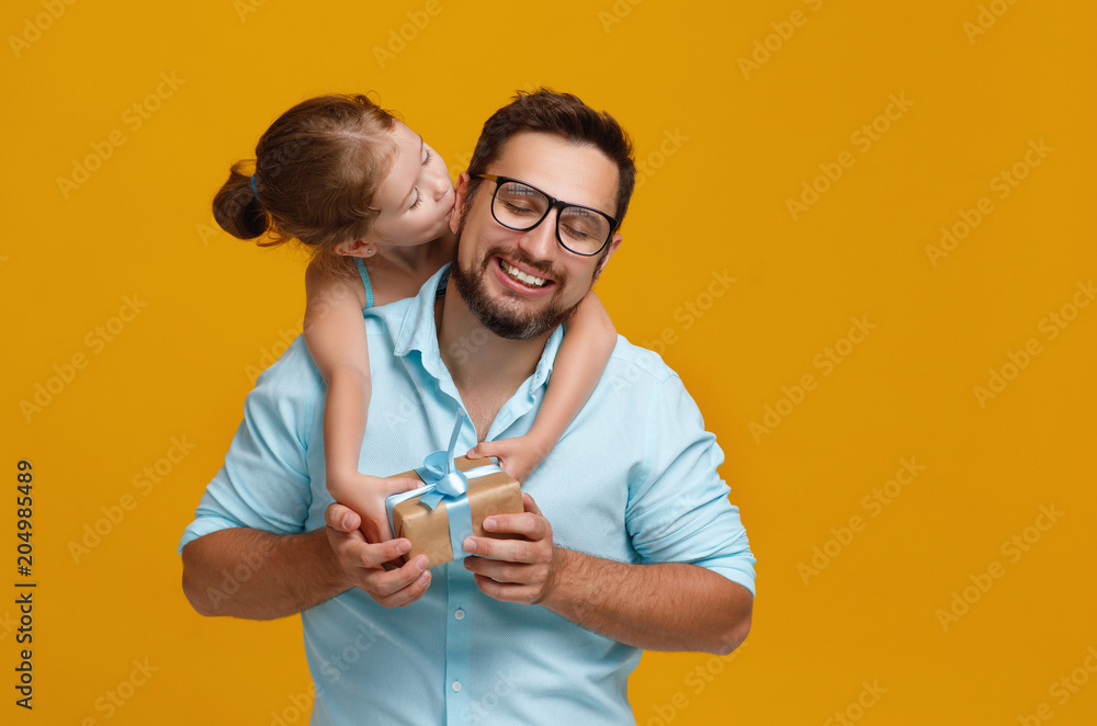 父亲节快乐！可爱的爸爸和女儿在黄色背景下拥抱。