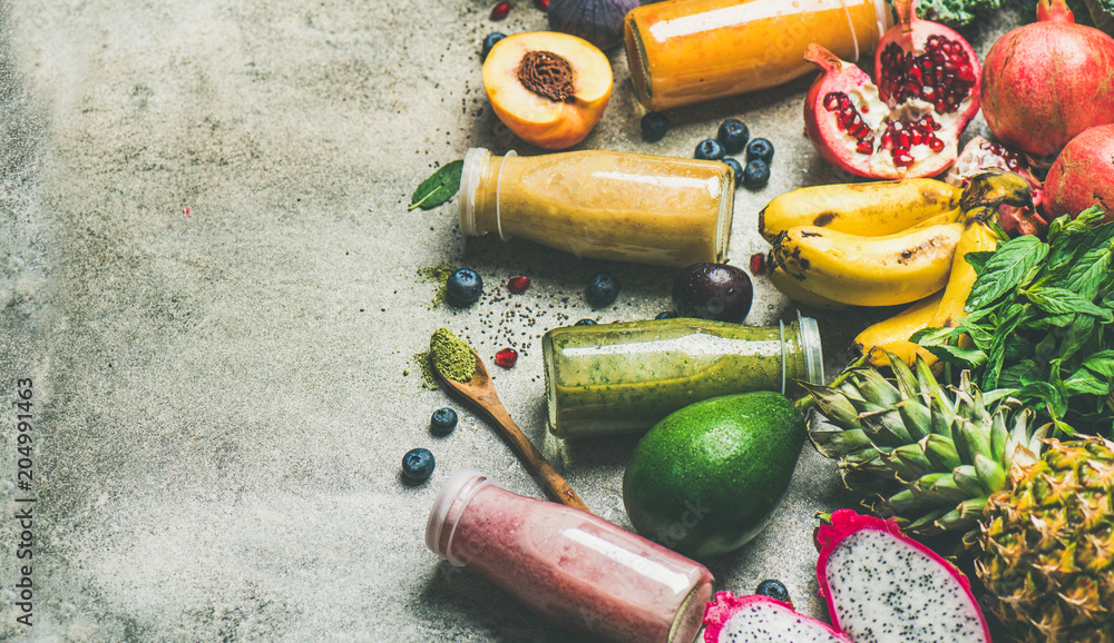 彩色冰沙装在瓶子里，混凝土背景上有新鲜的热带水果和超级食品，复制品