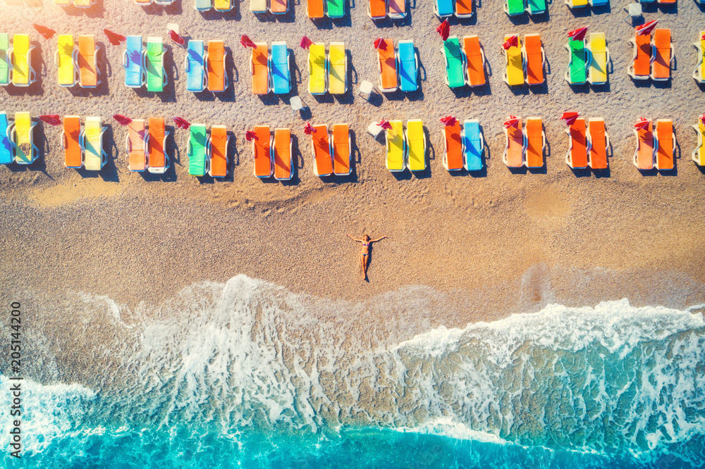 Aerial view of lying woman on the beach with colorful chaise-lounges. Young woman on the sea at suns