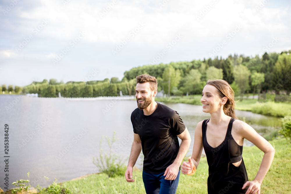 Couple in black sportswear running near the lake during the morning exercise