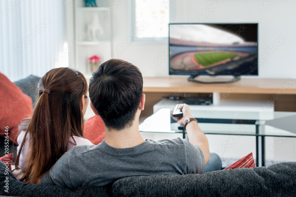 Rear view of Asian couple watching football at television in living room. Football festival concept.
