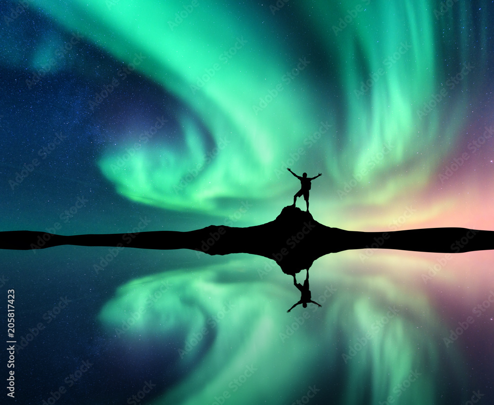 北极光和山上举起双臂的站立男子的剪影。挪威。Night la