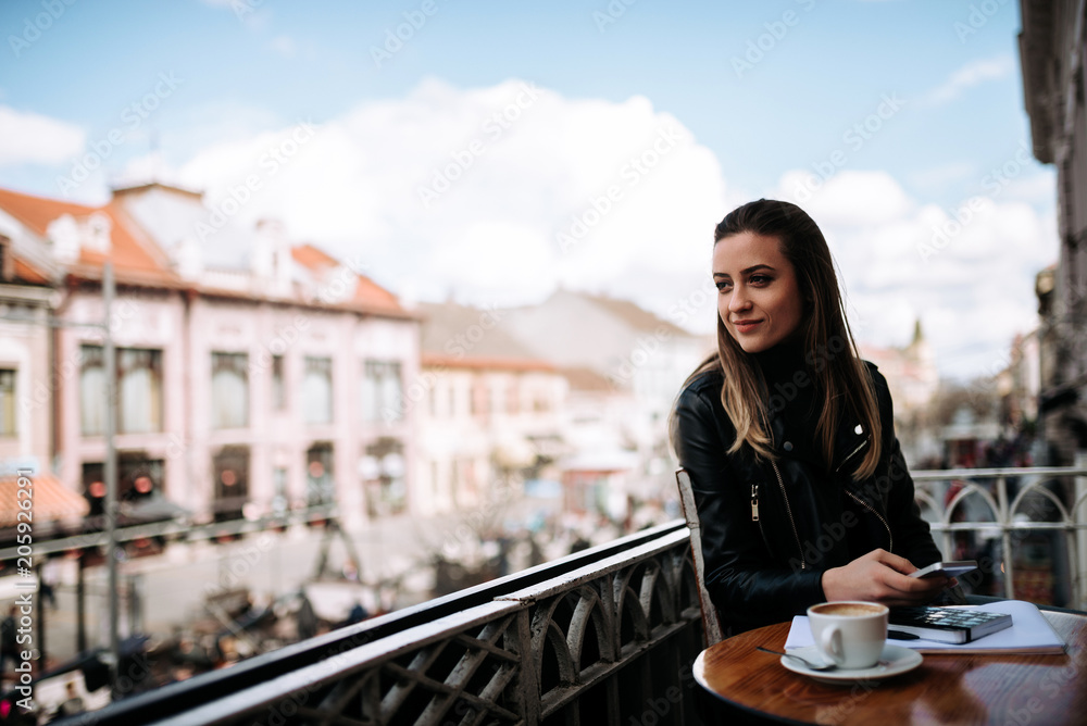 白日梦。可爱的微笑女孩坐在欧洲城市街阳台上的咖啡馆里。