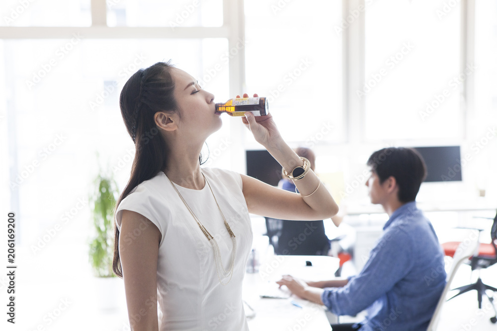 女性はオフィスで栄養ドリンクを一気に飲んでいる