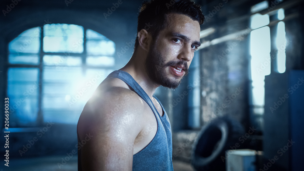 精疲力竭的肌肉男在健身房锻炼后看着镜头。汗水从他身上滴下来