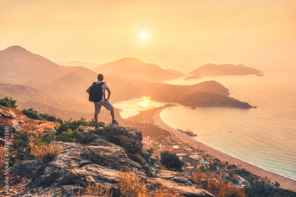 背着背包，站在岩石顶部，眺望海岸和山脉的年轻运动型男子