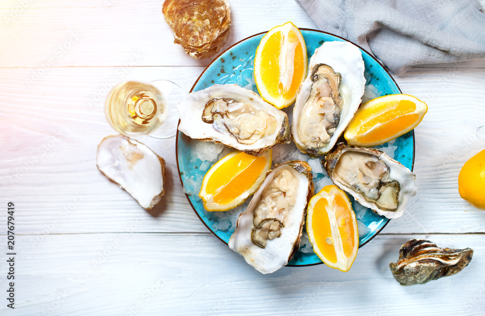蓝色盘子里的新鲜牡蛎特写，餐厅里的餐桌上有牡蛎、柠檬和香槟。