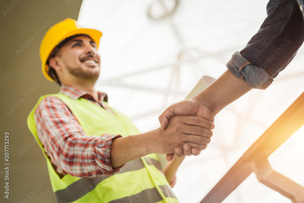 戴着防护帽和背心的工程施工人员在工作时握手