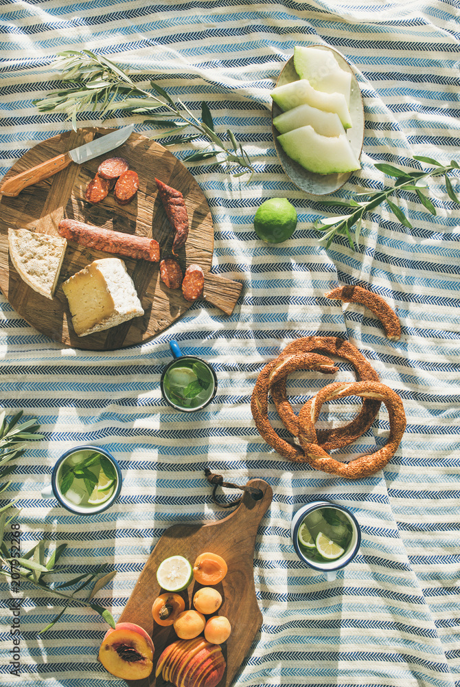 夏季野餐套餐，在条纹毯子上放上水果、奶酪、香肠、百吉饼和柠檬水。