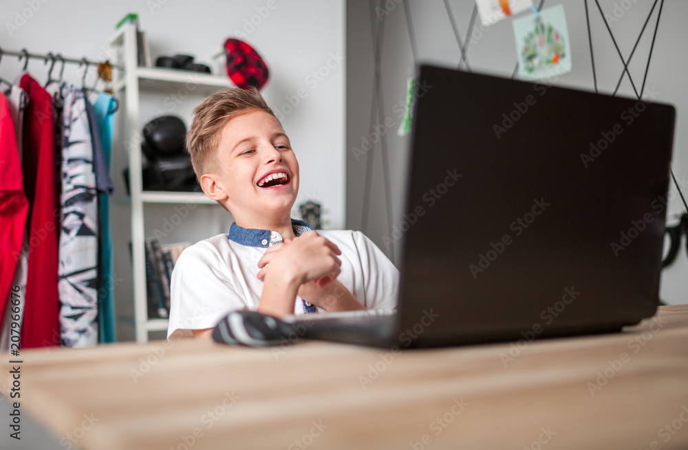 大笑的小男孩在家里的房间里用笔记本电脑看电影