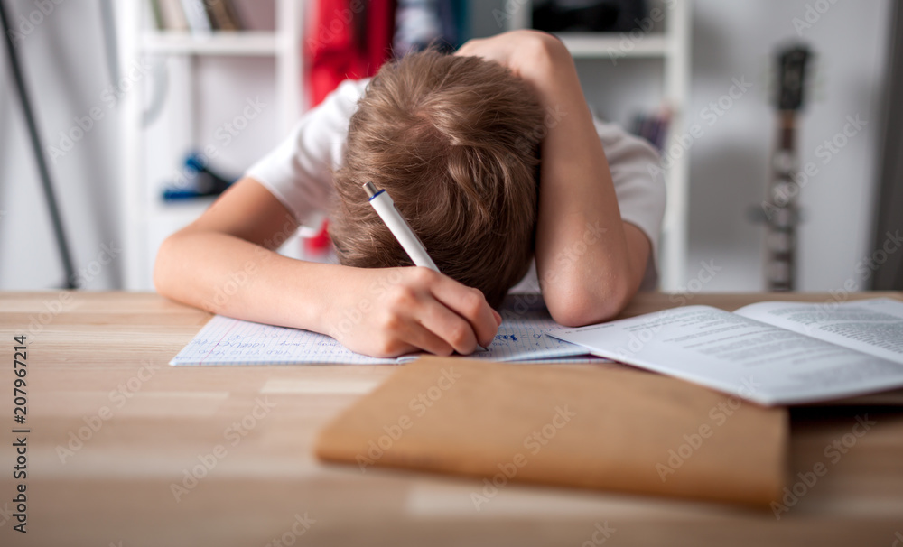 无聊而疲惫的十几岁男孩在房间的书桌上做作业