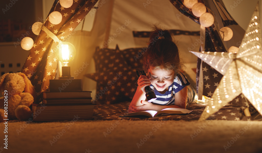快乐的小女孩在家里的帐篷里在黑暗中笑着看书