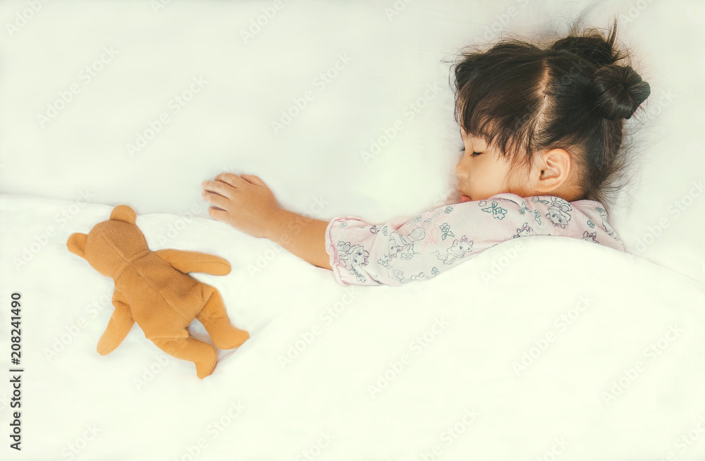 可爱的亚洲孩子和她的泰迪熊在白色床上睡觉