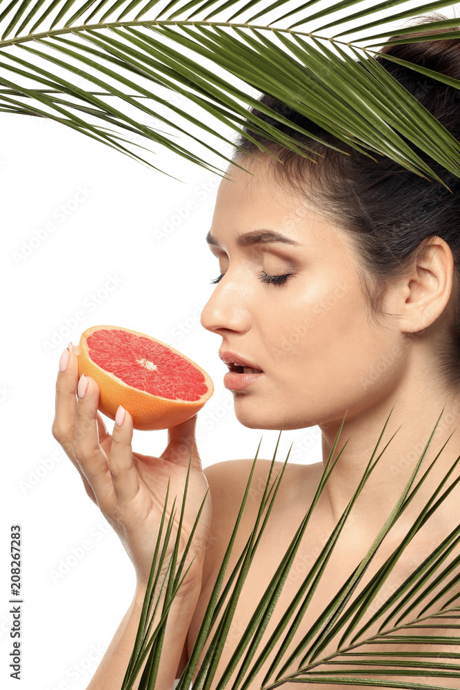 美丽的年轻女子，白色背景下有柑橘类水果和棕榈叶