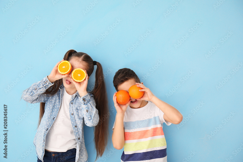 Funny little children with citrus fruit on color background
