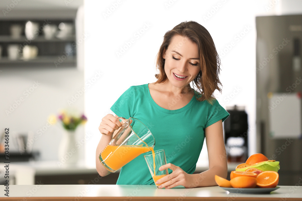 漂亮女人在厨房里把柑橘汁从罐子里倒进杯子里