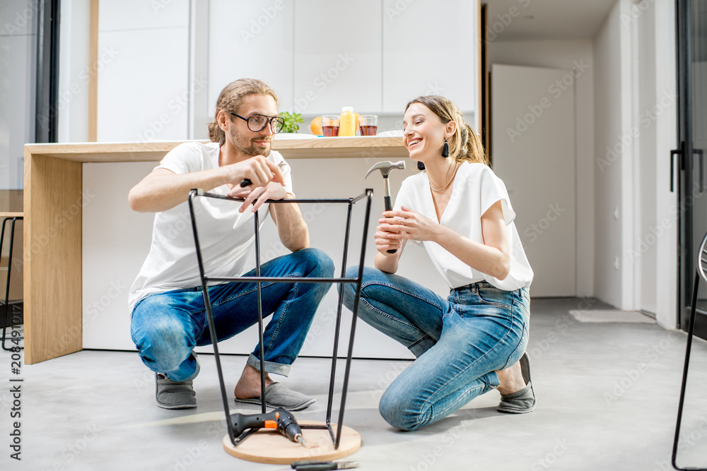 年轻可爱的夫妇在现代公寓的厨房里做家务，组装一把新椅子