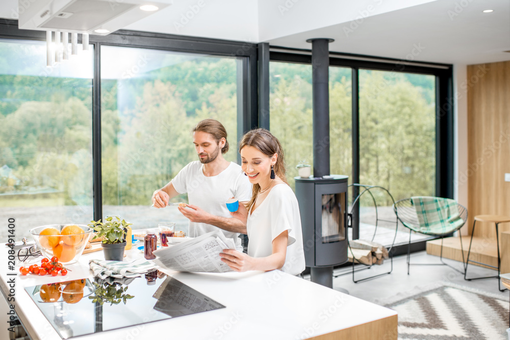 年轻夫妇在早餐时间坐在现代住宅内部的厨房里玩得很开心