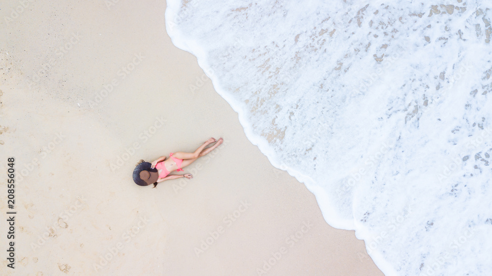 空中俯视图，穿着比基尼的年轻女子躺在沙滩和海浪上，年轻女子晒日光浴和放松