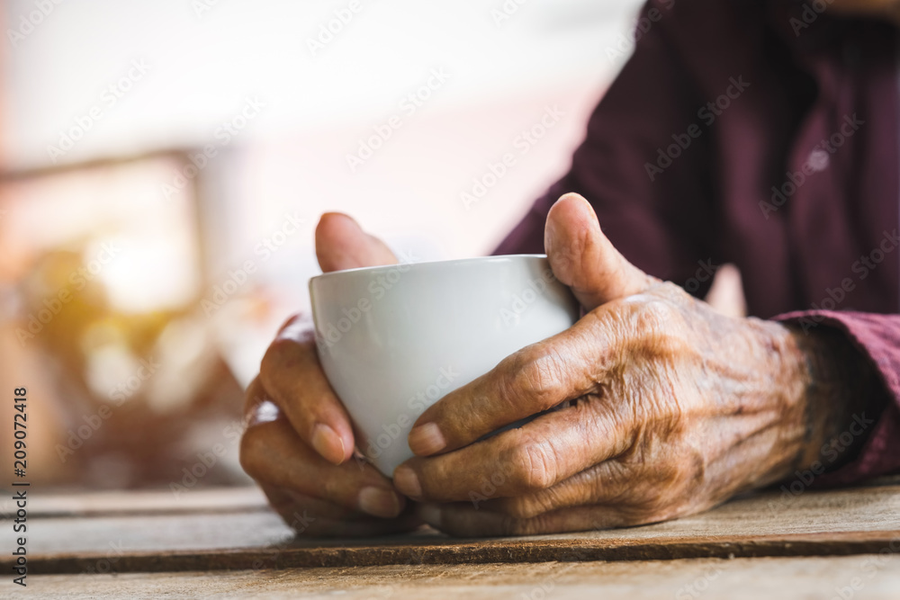 木头桌子上拿着一杯咖啡的老人的手。画风