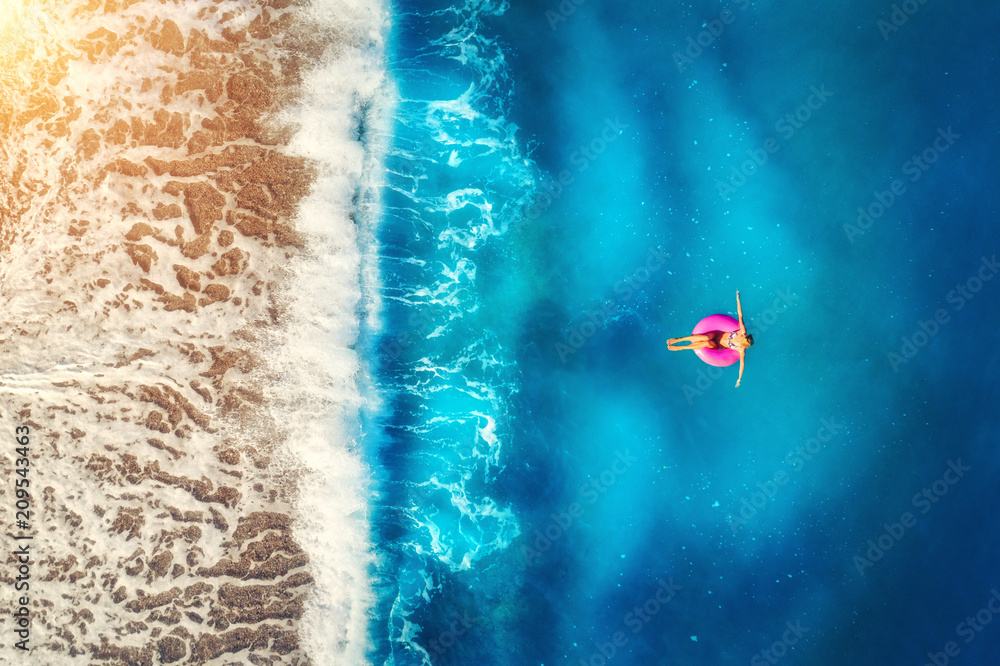 Eu透明的大海和美丽的海浪中，一名女子在粉色游泳圈上游泳的鸟瞰图