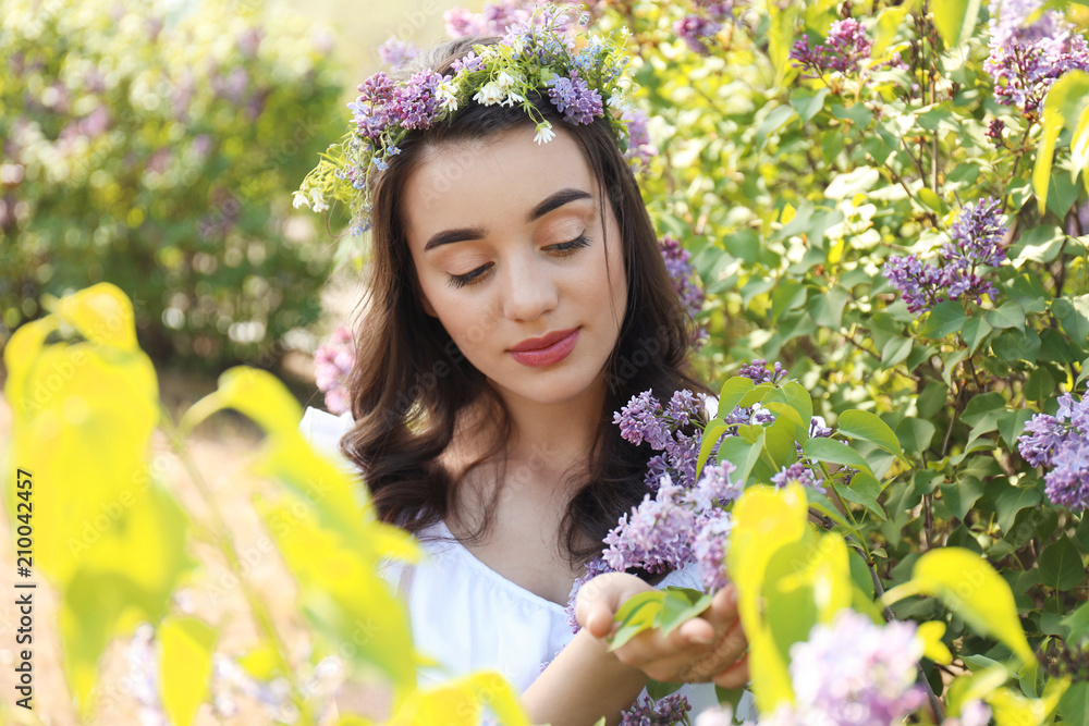 阳光明媚的春天，美丽的年轻女子在盛开的灌木旁戴着花环