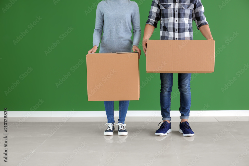 年轻夫妇在室内彩色墙附近拿着盒子。搬进新房子