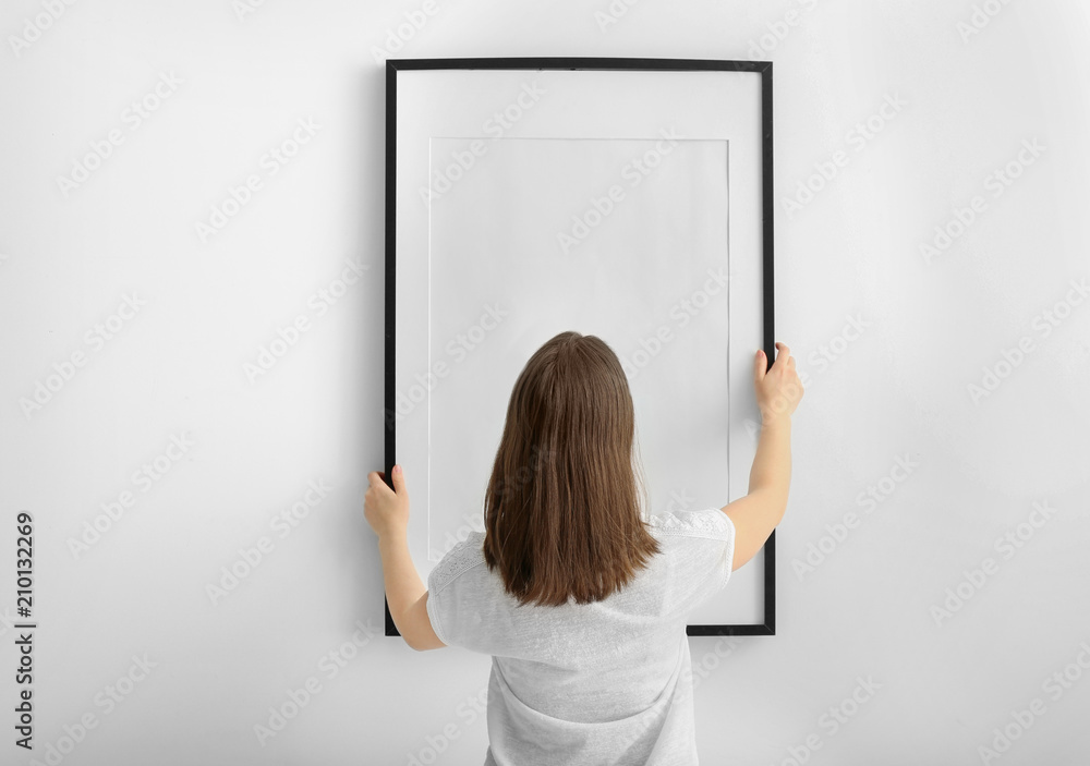 白墙上挂着空白相框的女人