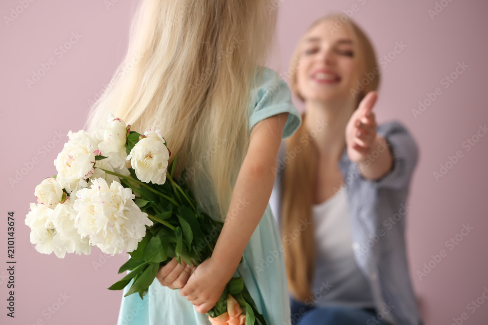可爱的小女孩在彩色背景下为母亲藏着一束花