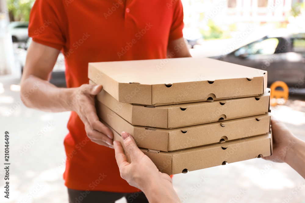 年轻男子在户外给女人送披萨盒。送餐服务