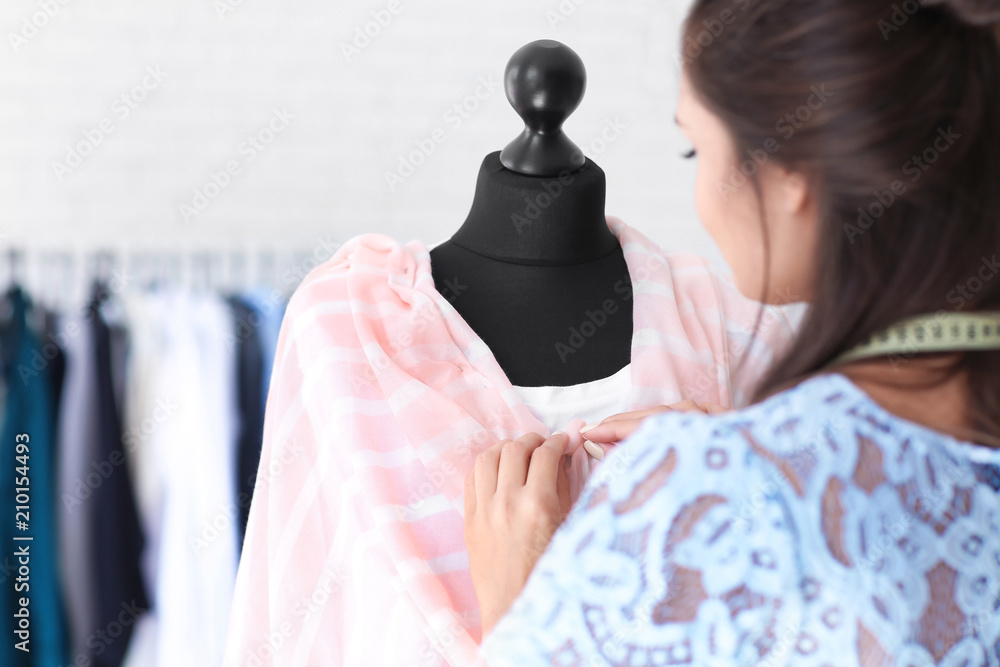 年轻的女裁缝在工作室的人体模型上穿着衬衫